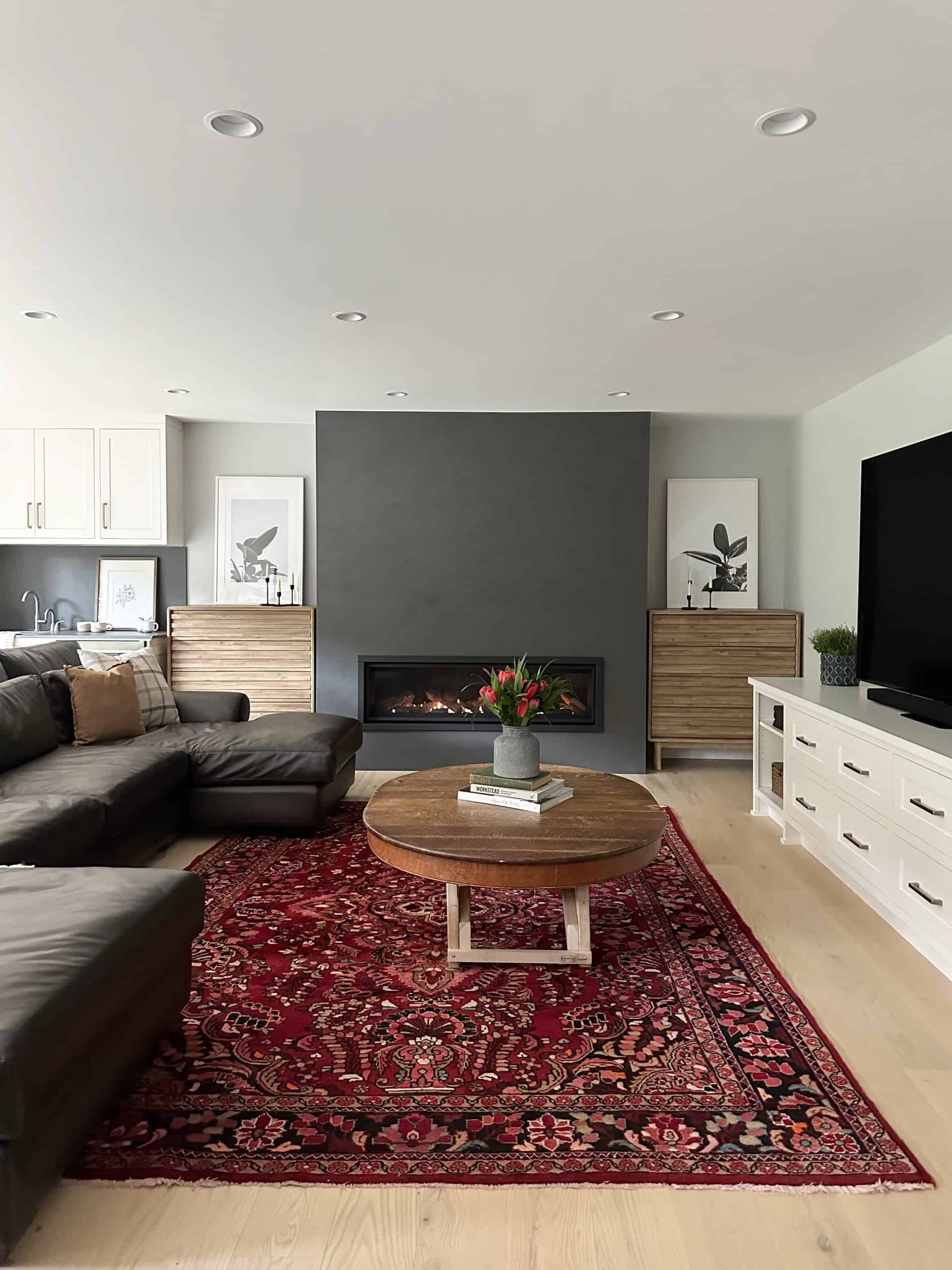 Modern living room with fireplace, dark accent wall, and red patterned rug in a bright open-plan.
