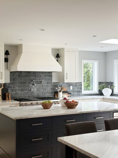 Modern kitchen with white cabinets, dark blue island drawers, and gray subway tile backsplash.
