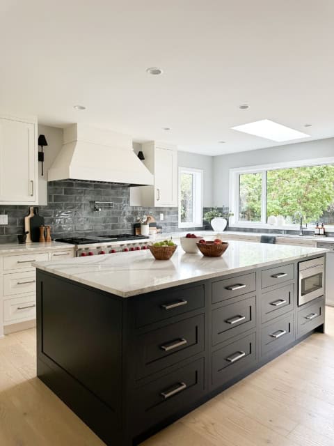 Modern kitchen with an oversized dark island and white cabinetry, bright natural light, and a brick-.
