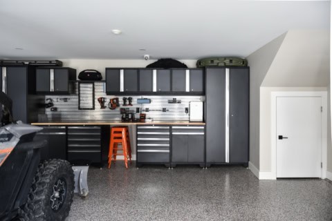 Garage workshop with dark gray cabinets, pegboard wall, and orange stool.