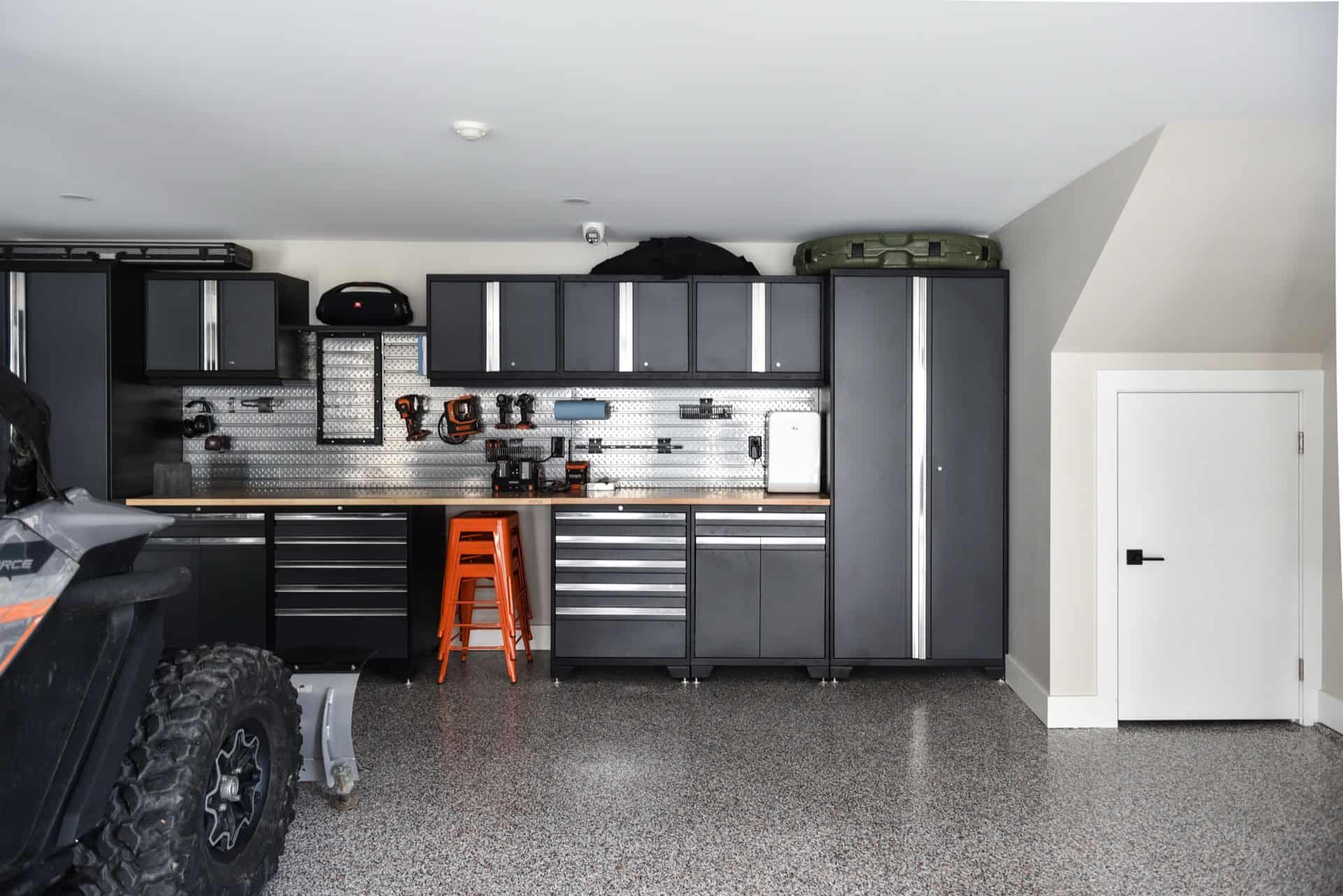 Garage workshop with dark gray cabinets, pegboard wall, and orange stool.