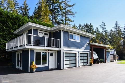Blue two-story home with a white balcony and large garage doors in a suburban setting.