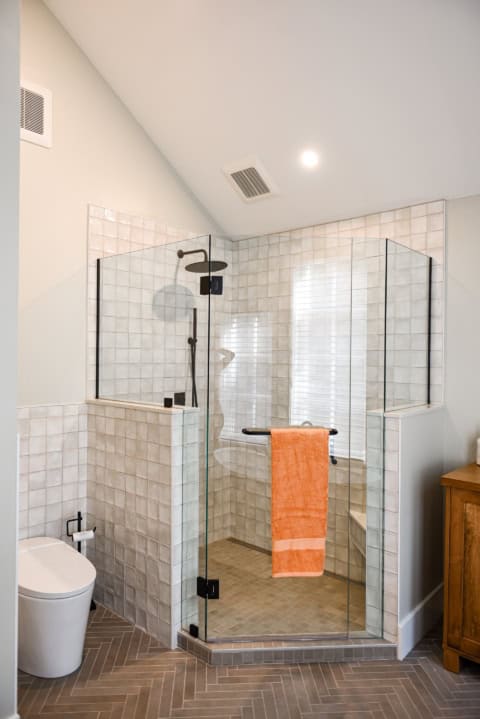 Modern glass shower enclosure with wall tiles and orange towel in contemporary bathroom.