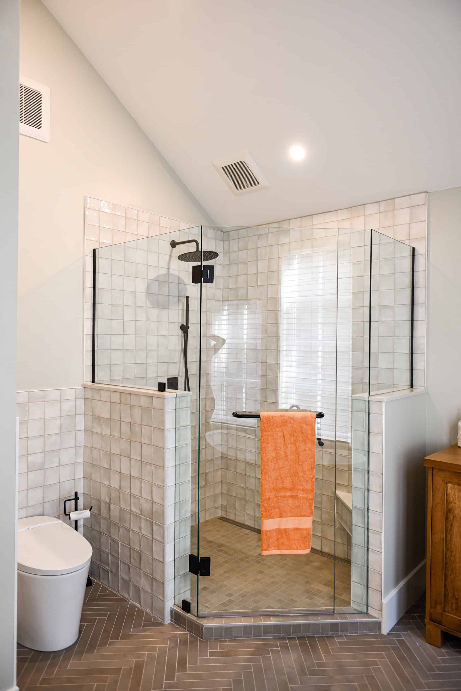 Modern glass shower enclosure with wall tiles and orange towel in contemporary bathroom.