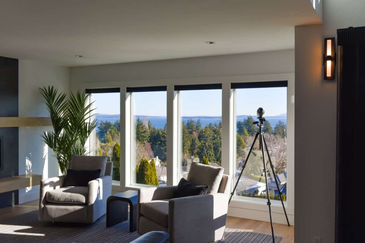 Bright living room with large windows, view of trees and lake, modern seating.