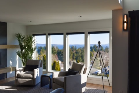 Bright living room with large windows, view of trees and lake, modern seating.