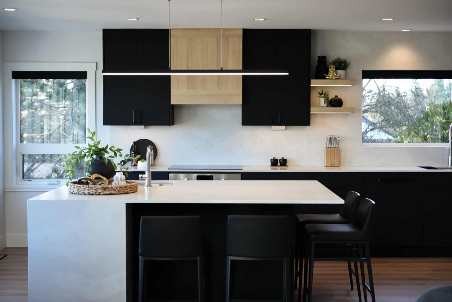 Modern kitchen with black cabinets, white island, and large windows.