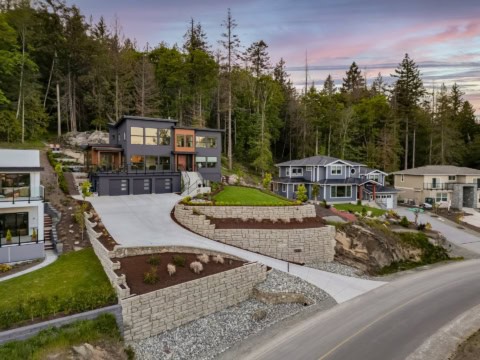 Victoria BC custom home by White Wolf Homes on hillside, modern dark exterior, stone retaining walls.