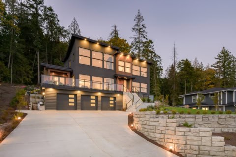 Modern custom home by White Wolf Homes in Victoria BC with dark facade, large windows, and driveway.