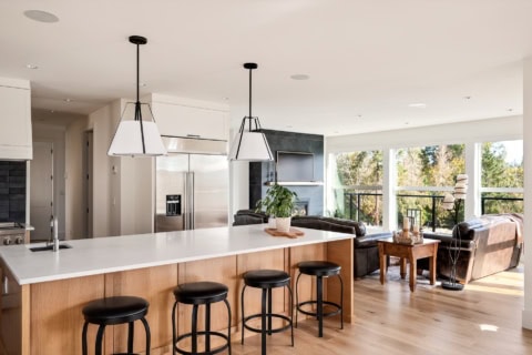 Open-concept kitchen island with four stools and a bright living area with large windows in a modern.