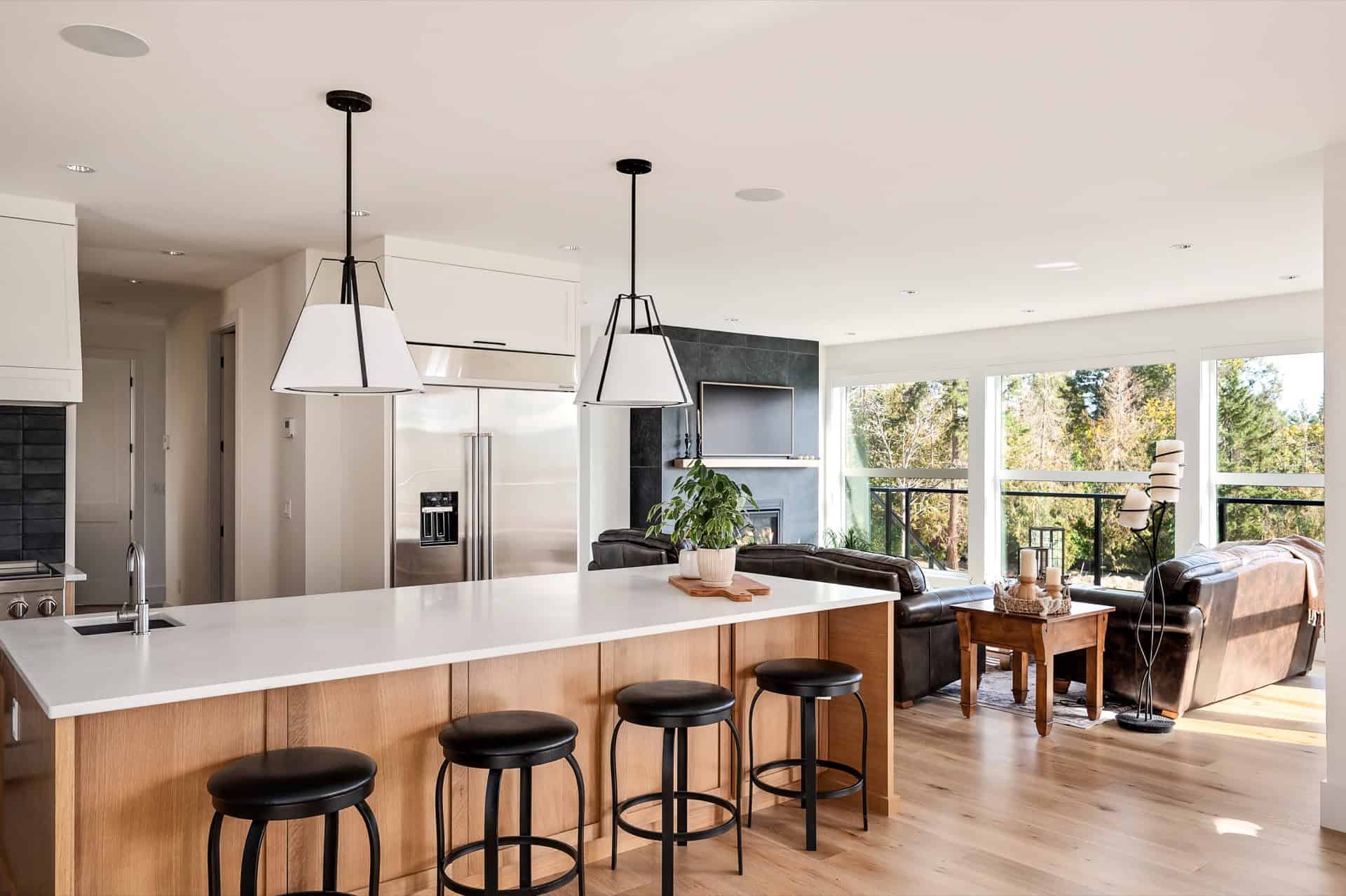Open-concept kitchen island with four stools and a bright living area with large windows in a modern.